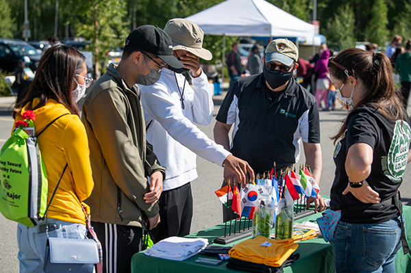 Brian Tang, Maezelle Tacas, and Lawrence Giron check out the Multicultural Student Services table with Student Success Coordinator Leo Medal at ɫƬ's Fall 2021 Campus Kickoff outside the Alaska Airlines Center.